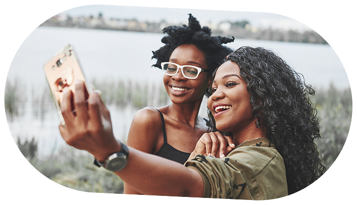 Two ladies taking a selfie in the outdoors with their cell phone.