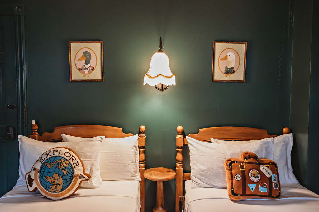 Two twin beds with travel-themed pillows and vintage decor.