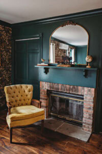 A vintage-style living room corner featuring a brick fireplace, an ornate mirror, and a mustard-yell.