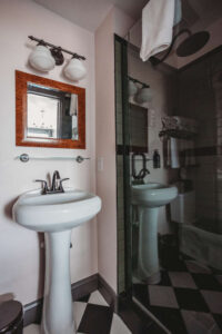 Bathroom with pedestal sink, mirror, and glass shower enclosure.
