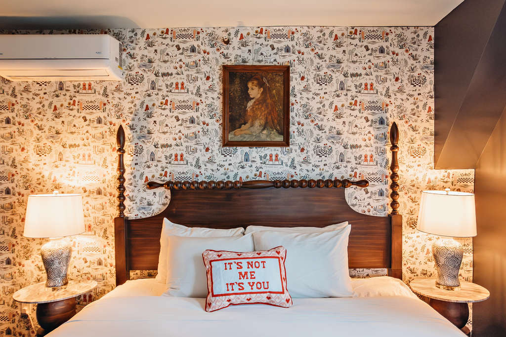 A charming hotel room featuring a wooden bed, vintage wallpaper, and warm lighting.