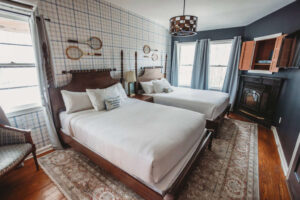 A charming hotel room featuring two beds, vintage decor, and a fireplace.
