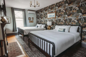 A stylish hotel room featuring two beds, patterned wallpaper, and modern decor.