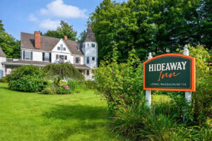A welcoming sign for Hideaway Inn in Lenox, Massachusetts, surrounded by greenery.