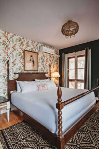 A charming bedroom featuring floral wallpaper, a wooden bed, and natural light from the window.