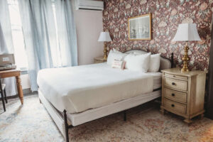 A cozy hotel room featuring a large bed, vintage nightstands, and classic decor.