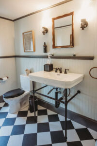 Bathroom featuring a vintage-style mirror, wall sconces, and a black-and-white checkered floor.