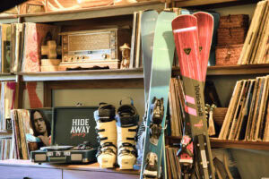 A collection of vintage skis, snowboards, books, and a radio on a wooden shelf.