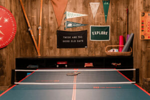A ping pong table with paddles and balls in a rustic game room setting.