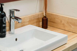 A modern bathroom sink with wooden countertop, soap dispenser, and decorative bottle.