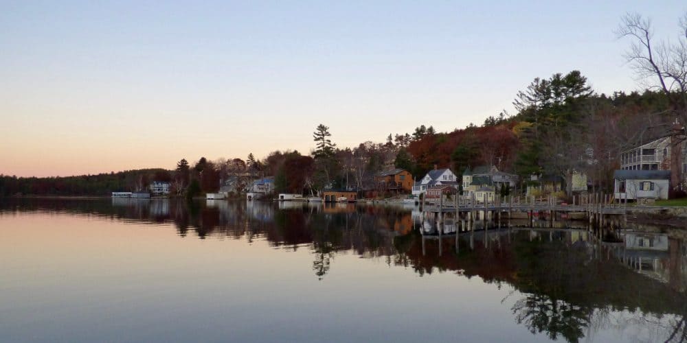 Scenic view of Lake George with houses, trees, and calm water during sunset.