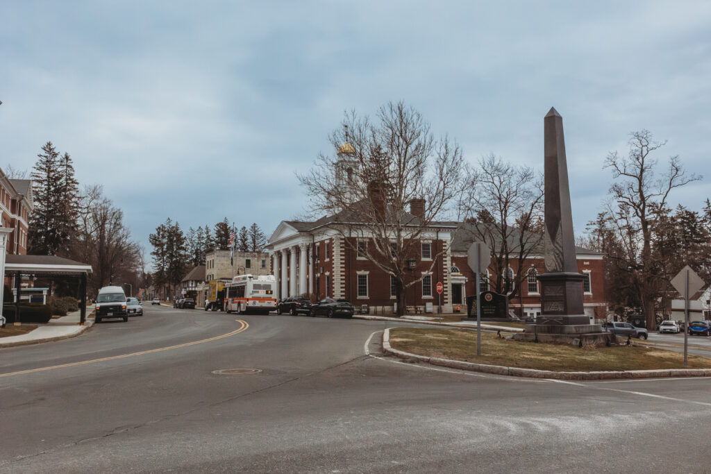 View of a small town square featuring a tall monument, historic architecture, and leafless trees.