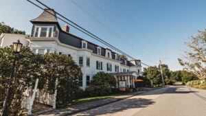 A historic inn with white exterior, black roof, and lush greenery in a quiet neighborhood.