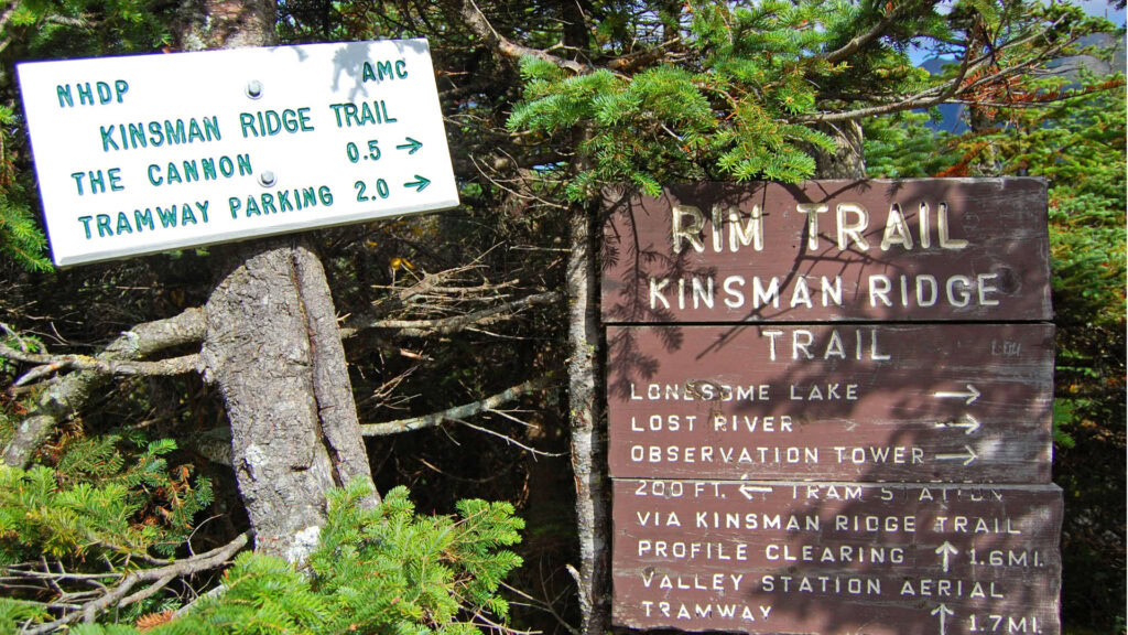 Trail signs for Kinsman Ridge, The Cannon, and Tramway Parking in a wooded area.