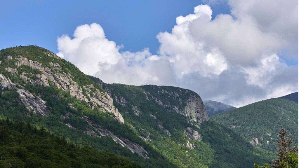 Beautiful mountain view with green trees and rocky cliffs under a partly cloudy sky.
