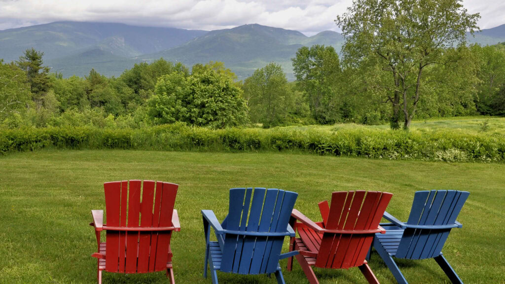 Colorful Adirondack chairs on a lush green lawn with mountains in the background.