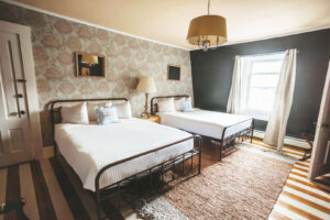 Hotel room with two beds, patterned wallpaper, and natural light from window.