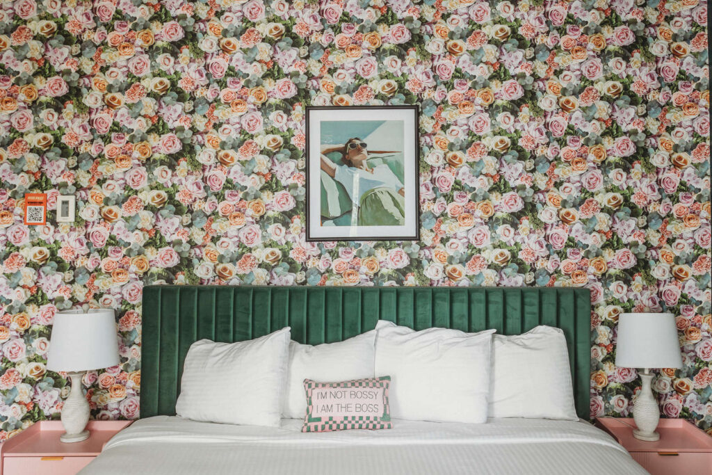 Bedroom with floral wallpaper, green headboard, and framed art.