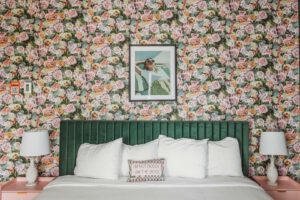 Bedroom with floral wallpaper, green headboard, and framed art.