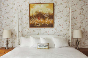 Bedroom with floral wallpaper, white bed, and framed art above headboard.