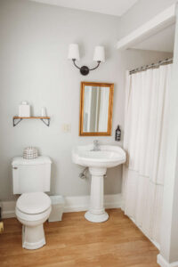 Bright bathroom with white sink, toilet, mirror, and curtain.