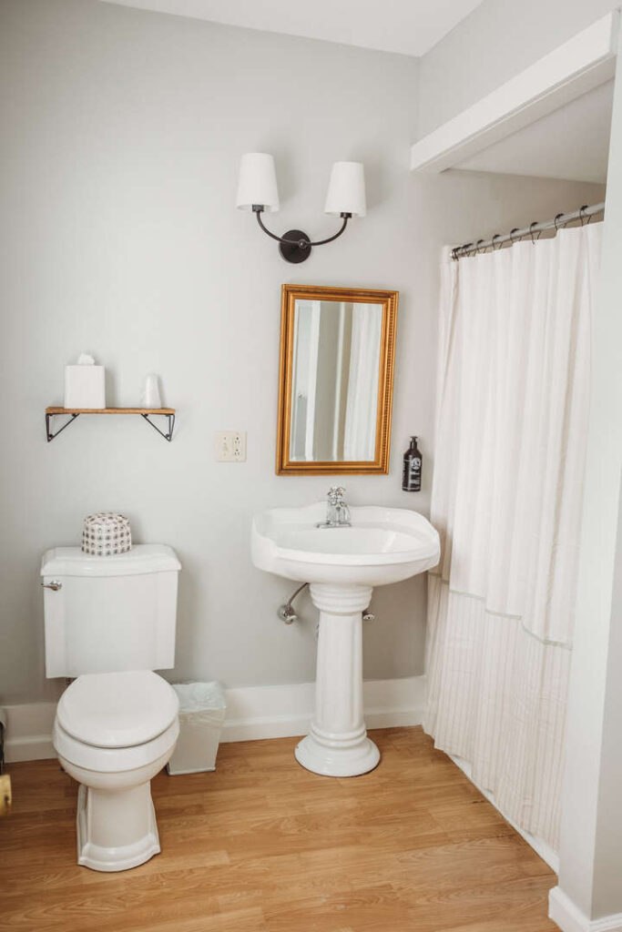 Bright bathroom with white sink, toilet, mirror, and curtain.