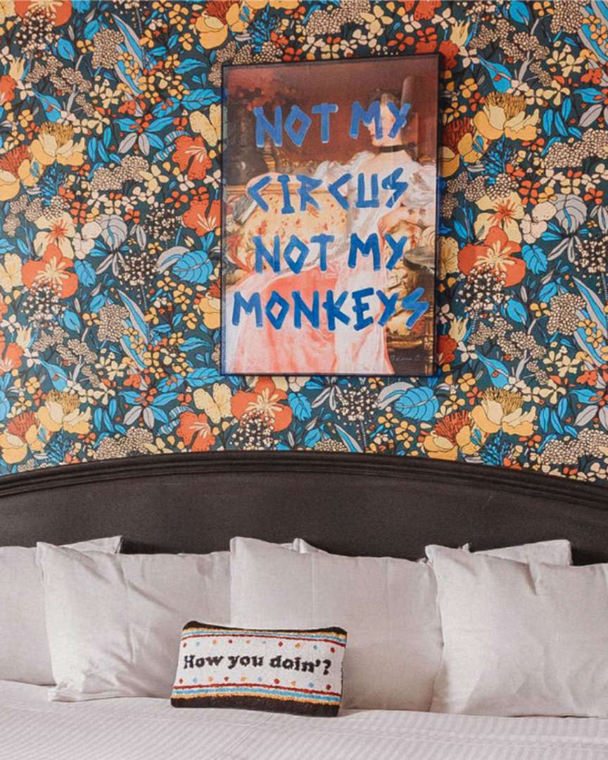 Hotel room with floral wallpaper, graffiti art, and a bed with a pillow.