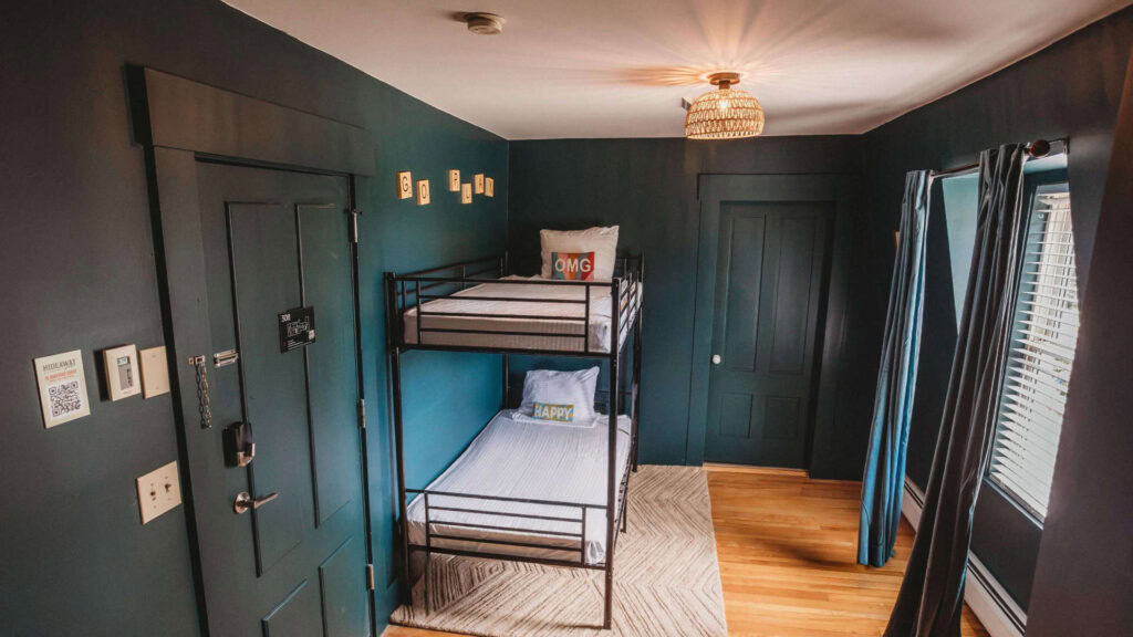 Interior of a hotel room with dark teal walls, bunk beds, and large windows with curtains.