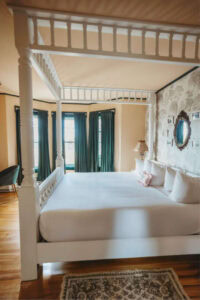 Bright bedroom with four-poster bed, vintage decor, and large windows.