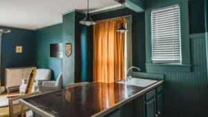 Interior of a hotel room featuring a kitchen island, window with blinds, and colorful curtains.
