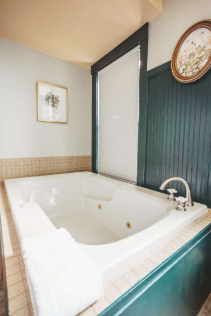 Indoor hot tub with white towel and window with blinds in the background.