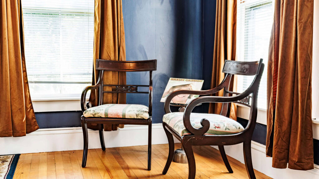 Two vintage-style chairs with floral cushions in a bright room with blue walls and gold curtains.