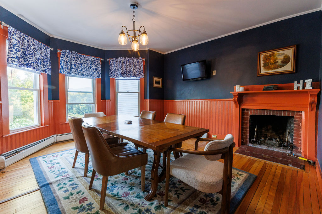 Warm dining room with wooden table, chairs, fireplace, and large windows.